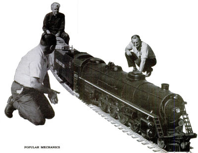 Seymour F. Johnson rides astride diesel switch engine as he pushes steam locomotive and train over new section of 1.5 inch scale track to check its accuracy.