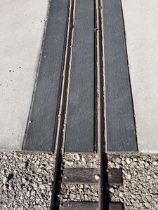 A typical grade crossing on the Lakes Park Railroad. A plastic 2x6 in the middle, with aluminum rail turned on its side with the head of the rail contacting the web of the steel rail.