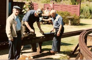 Carl Purinton (right) watches Charlie Smith (center) pump water into the boiler of Carl's little Mogul. Gilbert Greenberg on the left watches Bob Hornsby take pictures. Taken at Charlie Puriton's track (Carl's son) in 1985.