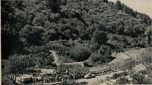 G.G.L.S. track nestled in canyon at Redwood Region Park at Oakland, California. Track is in the form of a figure eight. People are seen crowded around the steaming tracks and at the extreme lower left is the portable lunch wagon where refreshments were served. Photo by Paul Erbacher.