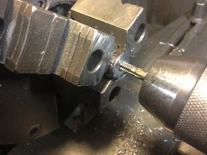 The three phase power is turned off to the lathe, the head is disengaged, and the part is threaded to 1/4-20 by manually turning the three jaw chuck. The tap is held in the tailstock. I like to lock the tailstock and gently feed the tap into the part until the threads are well established (about 2 or three turns). Then I losen the tail stock and let the the part "pull in" the tap the rest of the way. The threads are cut all the way through the 1/2 inch long part.